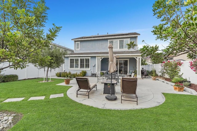 rear view of house with solar panels, a patio, and a lawn