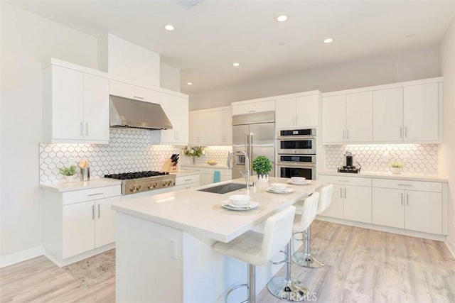 kitchen featuring white cabinetry, sink, stainless steel appliances, an island with sink, and extractor fan