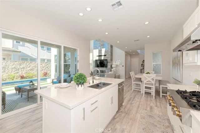 kitchen featuring white cabinetry, dishwasher, sink, an island with sink, and light wood-type flooring