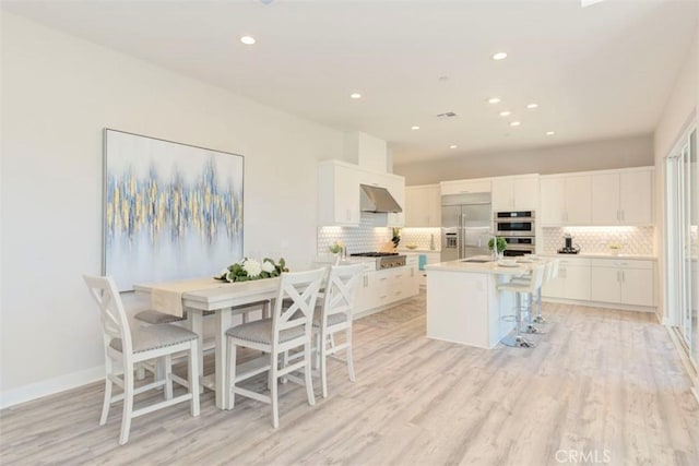 kitchen with an island with sink, a kitchen bar, white cabinets, exhaust hood, and appliances with stainless steel finishes