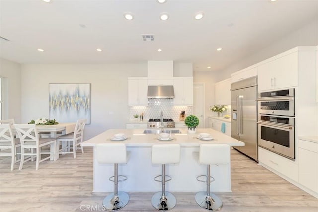 kitchen with a kitchen bar, white cabinetry, range hood, and appliances with stainless steel finishes