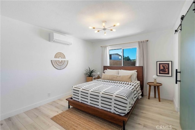 bedroom featuring a wall mounted air conditioner, a chandelier, a barn door, and light hardwood / wood-style flooring