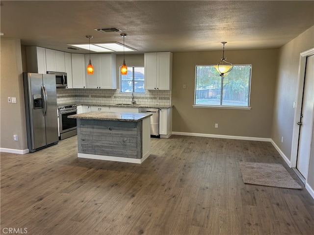 kitchen featuring white cabinetry, stainless steel appliances, light stone countertops, and decorative light fixtures