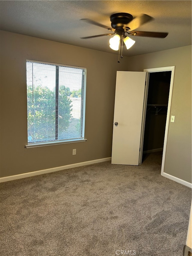 unfurnished bedroom featuring carpet floors, a closet, a spacious closet, a textured ceiling, and ceiling fan