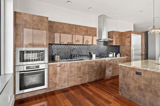 kitchen featuring wall chimney range hood, sink, hanging light fixtures, dark hardwood / wood-style flooring, and stainless steel appliances