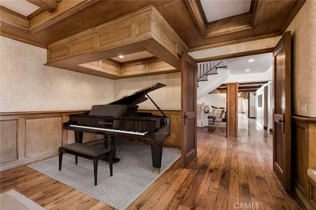 sitting room featuring wood-type flooring, a wainscoted wall, coffered ceiling, and ornamental molding