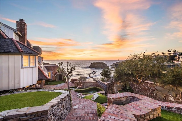 patio terrace at dusk featuring an outdoor fire pit and a water view