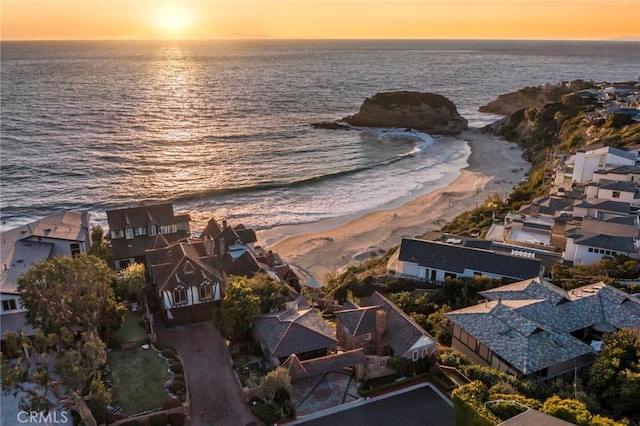 aerial view at dusk featuring a view of the beach and a water view