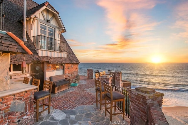 patio terrace at dusk with a bar, a water view, a view of the beach, and a fireplace