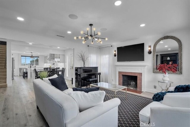 living room with a chandelier, a fireplace, light hardwood / wood-style floors, and sink