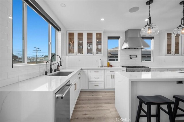 kitchen featuring appliances with stainless steel finishes, tasteful backsplash, sink, wall chimney range hood, and white cabinets