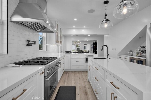 kitchen with white cabinetry, sink, stainless steel appliances, wall chimney range hood, and light hardwood / wood-style flooring