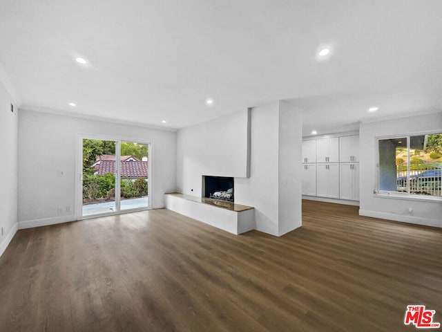 unfurnished living room featuring crown molding, plenty of natural light, and dark wood-type flooring