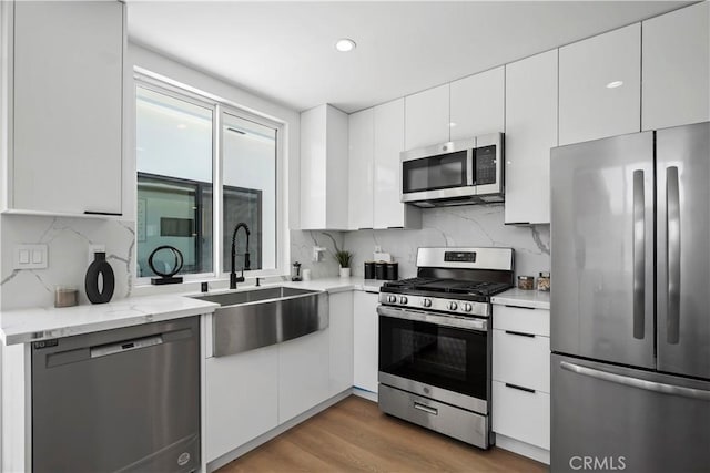 kitchen featuring sink, stainless steel appliances, backsplash, white cabinets, and hardwood / wood-style flooring