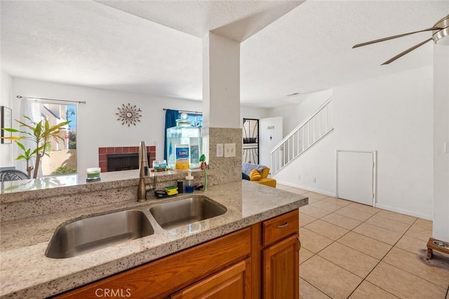 kitchen with light stone counters, ceiling fan, sink, a tile fireplace, and light tile patterned floors