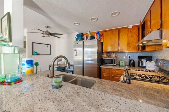 kitchen with ceiling fan, sink, stainless steel appliances, light stone counters, and a textured ceiling