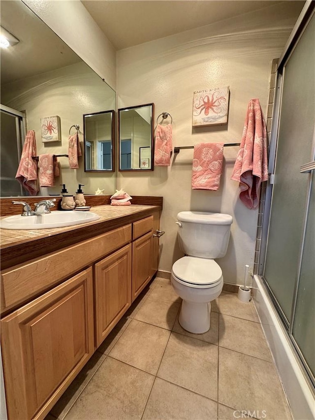 bathroom featuring toilet, vanity, a shower with door, and tile patterned flooring