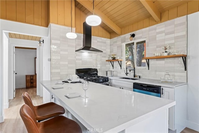 kitchen featuring tasteful backsplash, decorative light fixtures, gas stove, white cabinetry, and wall chimney exhaust hood