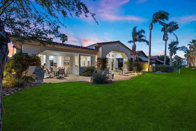 back house at dusk featuring a patio area and a lawn