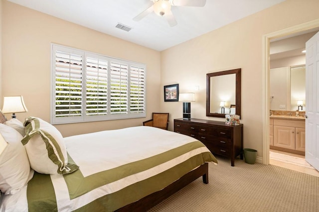 bedroom with ceiling fan, ensuite bathroom, and light carpet