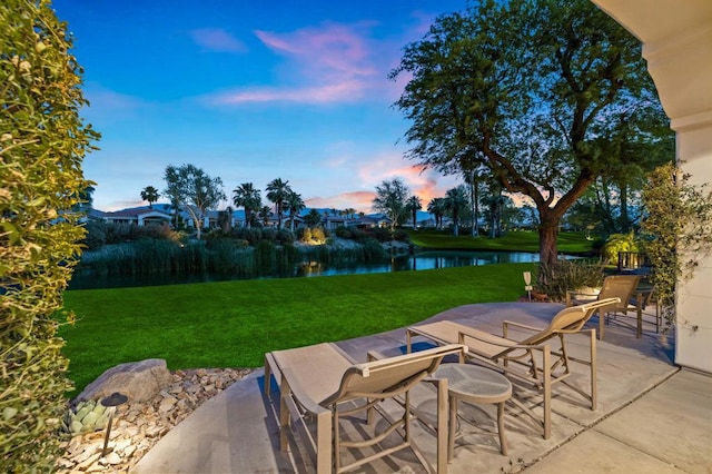 patio terrace at dusk featuring a lawn and a water view