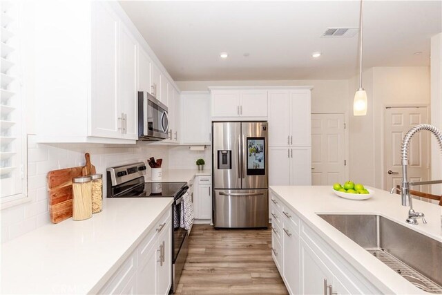 kitchen featuring appliances with stainless steel finishes, sink, light hardwood / wood-style flooring, white cabinets, and hanging light fixtures