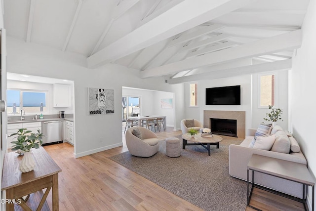 living room featuring a wealth of natural light, vaulted ceiling with beams, baseboards, and light wood-style floors