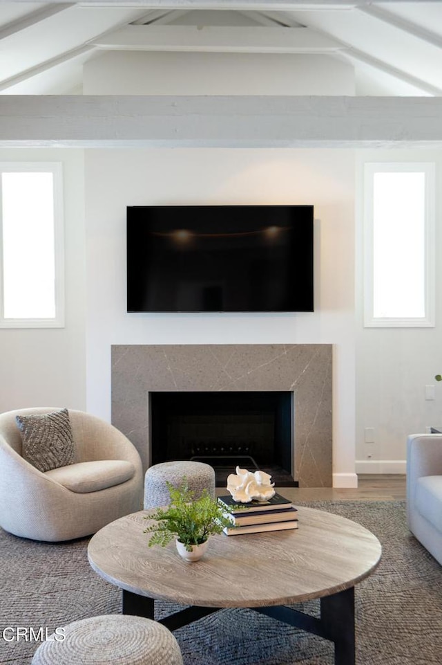 living area featuring lofted ceiling with beams, wood finished floors, a wealth of natural light, and a premium fireplace