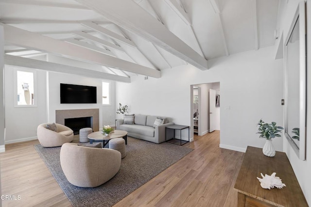 living area featuring baseboards, beam ceiling, light wood-style flooring, a fireplace, and high vaulted ceiling