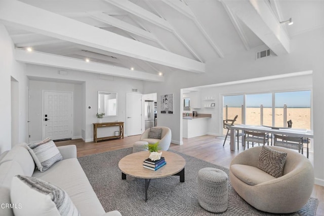 living area featuring visible vents, baseboards, beamed ceiling, light wood-style flooring, and high vaulted ceiling