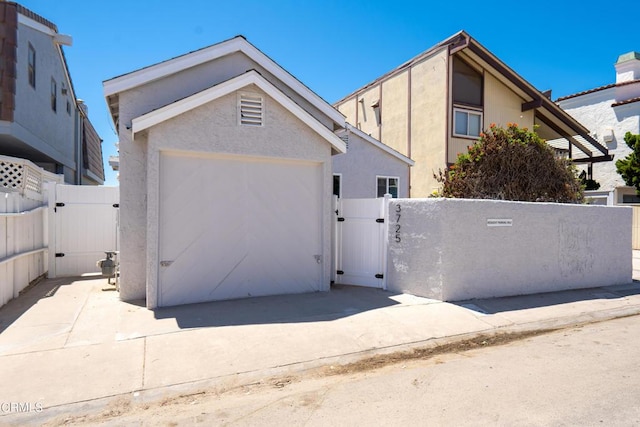 exterior space featuring stucco siding, fence, concrete driveway, and a gate