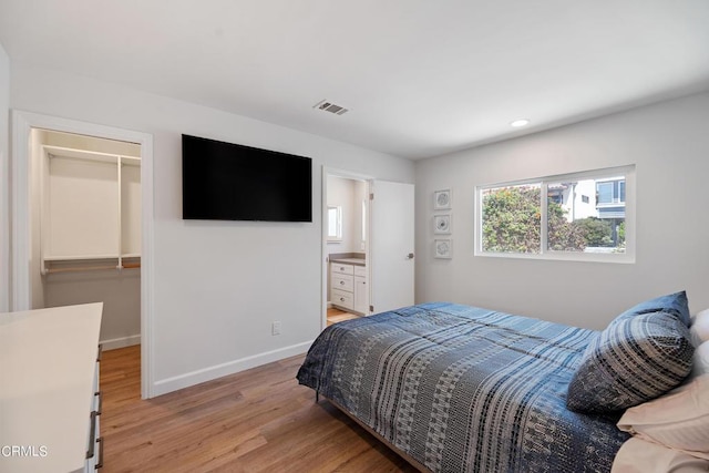 bedroom with a walk in closet, light wood-style floors, visible vents, and baseboards