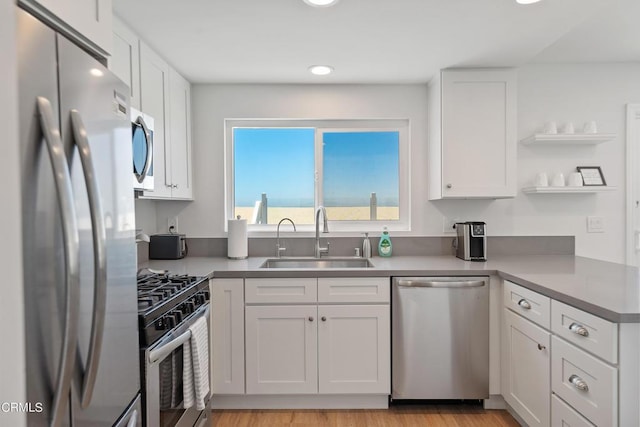 kitchen featuring light wood finished floors, a sink, appliances with stainless steel finishes, white cabinets, and open shelves