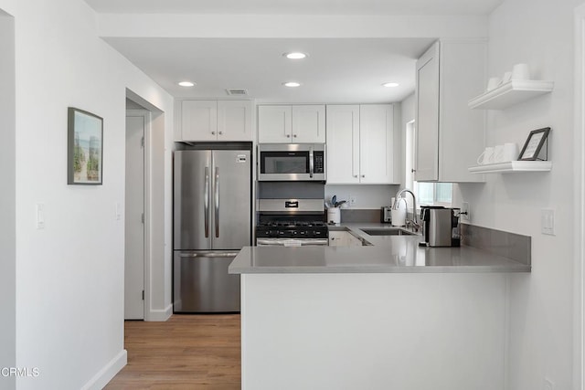 kitchen featuring a sink, open shelves, a peninsula, appliances with stainless steel finishes, and white cabinets