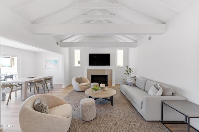 living area with a fireplace, light wood-type flooring, lofted ceiling with beams, and baseboards