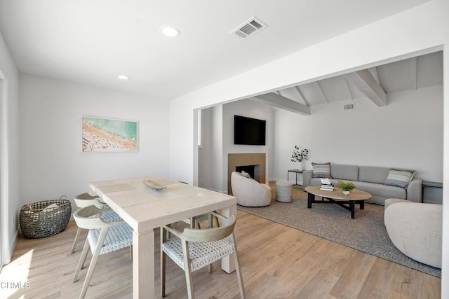 dining area featuring visible vents, light wood-style flooring, a fireplace, and beamed ceiling