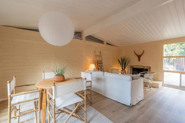 living room featuring vaulted ceiling with beams, light hardwood / wood-style floors, and brick wall