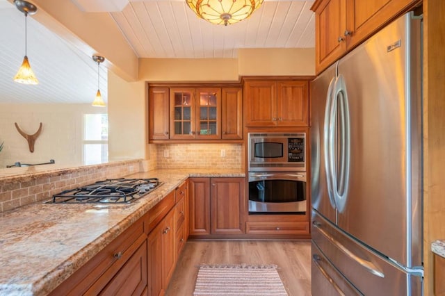 kitchen with light stone countertops, tasteful backsplash, light hardwood / wood-style flooring, decorative light fixtures, and appliances with stainless steel finishes