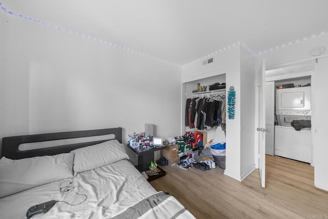 bedroom featuring stacked washing maching and dryer, a closet, visible vents, and wood finished floors