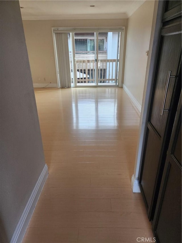 hall with light wood-style floors, crown molding, and baseboards
