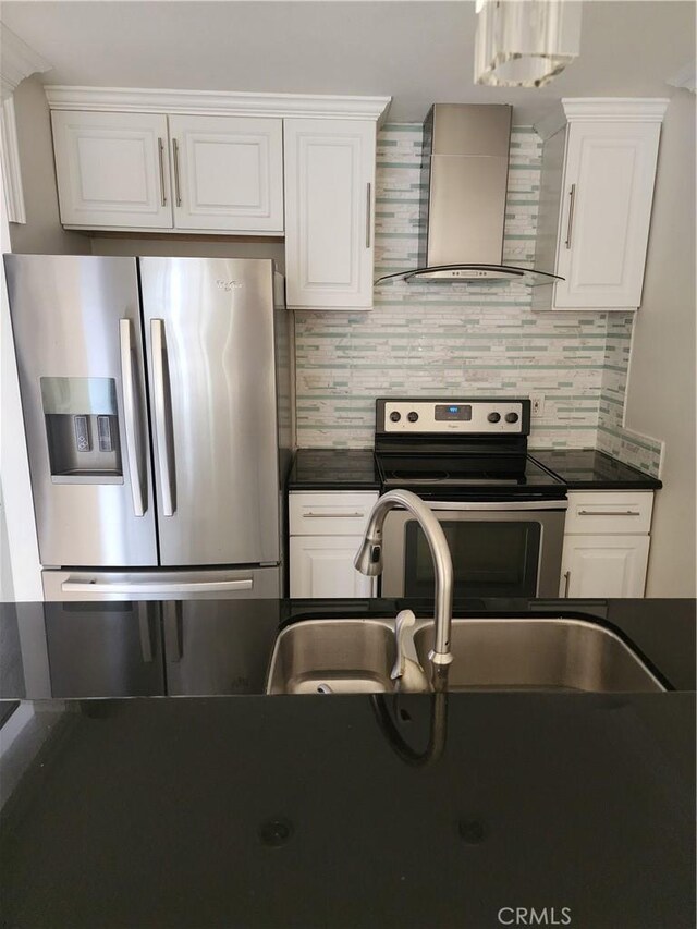 kitchen with white cabinets, dark countertops, appliances with stainless steel finishes, and wall chimney range hood