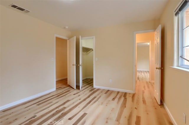 unfurnished bedroom with a spacious closet, light hardwood / wood-style flooring, and a closet