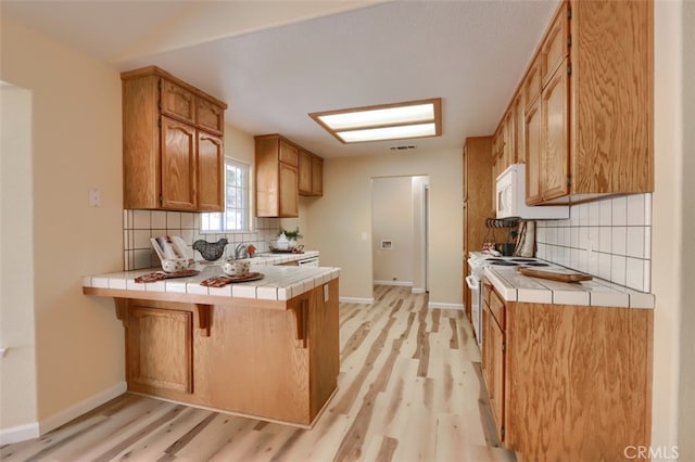 kitchen featuring decorative backsplash, a breakfast bar, light hardwood / wood-style floors, and tile counters