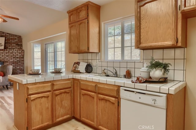 kitchen with kitchen peninsula, light hardwood / wood-style flooring, dishwasher, tile counters, and lofted ceiling