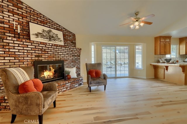 living area featuring ceiling fan, light hardwood / wood-style floors, lofted ceiling, and a brick fireplace