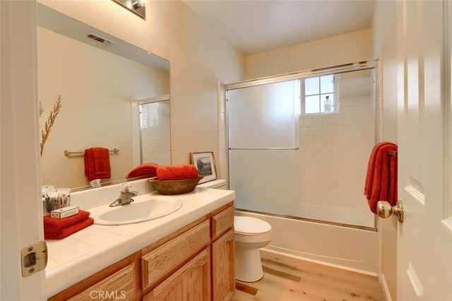 full bathroom featuring toilet, vanity, bath / shower combo with glass door, and hardwood / wood-style flooring