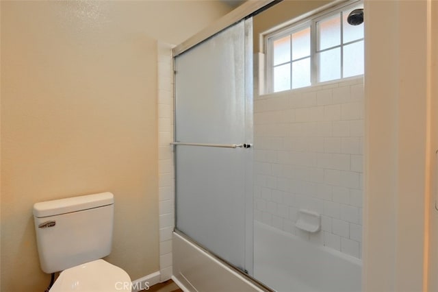 bathroom with toilet and bath / shower combo with glass door