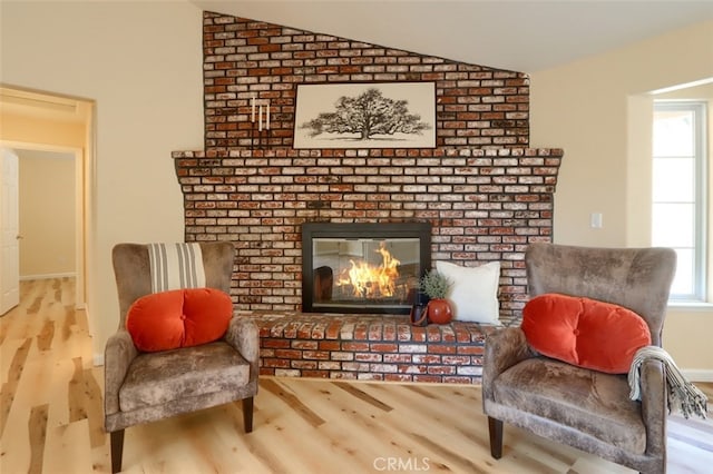 sitting room with light hardwood / wood-style floors, lofted ceiling, and a brick fireplace