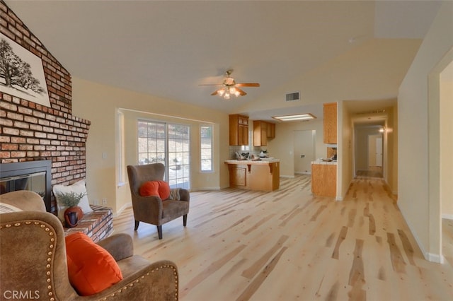 living room featuring ceiling fan, light hardwood / wood-style floors, lofted ceiling, and a brick fireplace