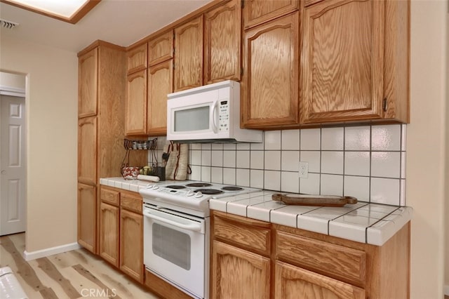 kitchen with tile countertops, decorative backsplash, light hardwood / wood-style floors, and white appliances